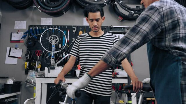 Owner shop asian senior man lift up bike out of stand and receive fixing cost from customer by scan qr code via mobile phone at cycle bike shop. Repair and maintenance concept