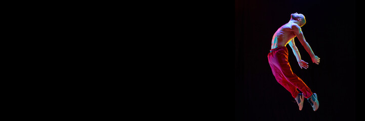Reborn. Young guy, talented, artistic dancer dancing breakdance on black studio background in neon...