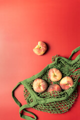 Pfirsiche in einem grünen Einkaufsnetz auf einem roten Tisch. Modern, Obst.