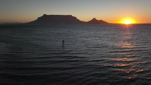 Cape Town South Africa windsurfers sailing windy surf wave Table Mountain drone aerial cinematic Lions Head sunset beach stunning mountain and ocean landscape orange gold sun on horizon back follow