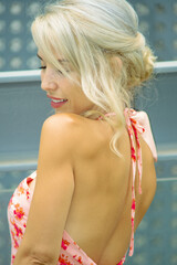 PRETTY GIRL WITH BLONDE HAIR AND WEARING A PINK AND RED DRESS IS SMILING AND TOUCHING HER HAIR WITH HER HAND