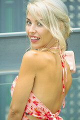 PRETTY GIRL WITH BLONDE HAIR AND WEARING A PINK AND RED DRESS IS SMILING AND TOUCHING HER HAIR WITH HER HAND