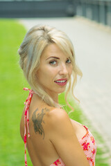PRETTY GIRL WITH BLONDE HAIR AND WEARING A PINK AND RED DRESS IS SMILING AND TOUCHING HER HAIR WITH HER HAND