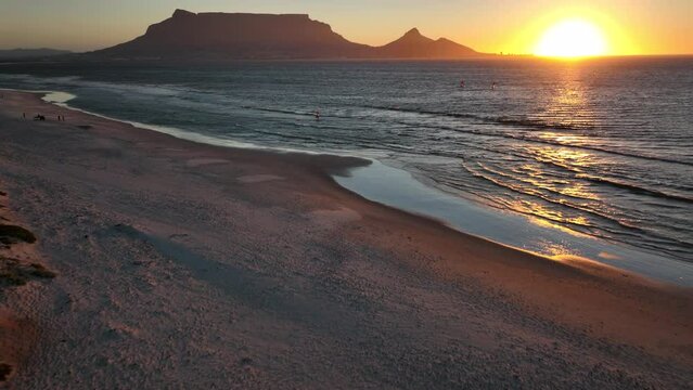 Cape Town South Africa windsurfers sailing windy surf wave Table Mountain drone aerial cinematic Lions Head sunset beach stunning mountain and ocean landscape orange gold sun horizon pan up fowward