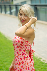 PRETTY GIRL WITH BLONDE HAIR AND WEARING A PINK AND RED DRESS IS SMILING AND TOUCHING HER HAIR WITH HER HAND