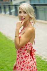 PRETTY GIRL WITH BLONDE HAIR AND WEARING A PINK AND RED DRESS IS SMILING AND TOUCHING HER HAIR WITH HER HAND