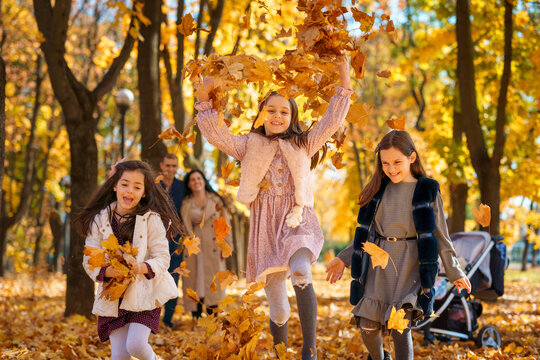 happy children playing together and scattering yellow leaves, portrait of big family in autumn city park, children running with armful of leaves, beautiful nature, bright sunny day