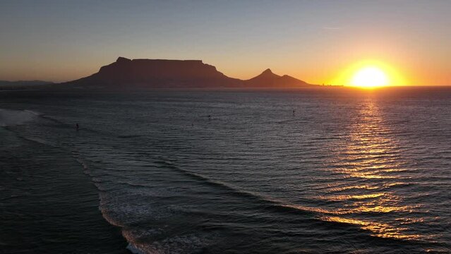 Cape Town South Africa windsurfers sailing windy surf wave Table Mountain drone aerial cinematic Lions Head sunset beach stunning mountain and ocean landscape orange gold sun on horizon backward pan