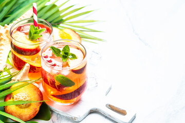 Peach cocktail, iced peach tea, fruit drink with palm leaves at tropical background.