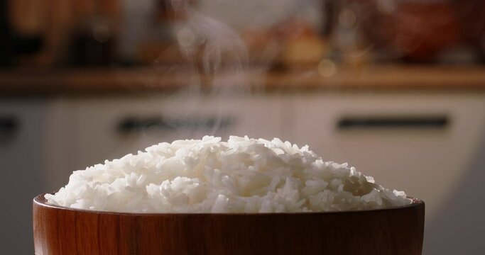 Hot white cooked rice steam bowl blurred kitchen background. Sticky rice after cooked. Asian Chinese Thai Japanese Indian dieting. Calm oriental lifestyle and culture