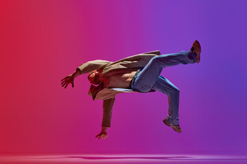 Dance show. Young guy in stylish clothes dancing hip hop, breakdance, contemp against pink purple studio background. Concept of art, street style dance, fashion, youth, hobby, dynamics, ad