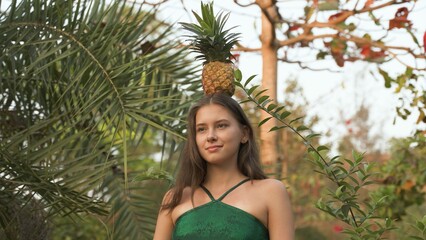 young woman stands in the park with a pineapple on her head