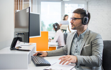 Confident male call center operator agent in headset with microphone consulting client online in...