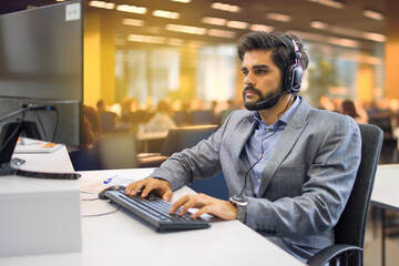 Handsome male technical support operator working at his workplace in call center office.