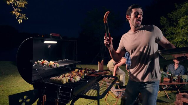 Man grilling barbecue for friends sitting in a circle campfire, Holiday and camping concept