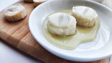 Sliced round Pieces of Banana on white plate and on wooden board on white background. Banana cooking, Close up. Delicious sweet fruit dessert