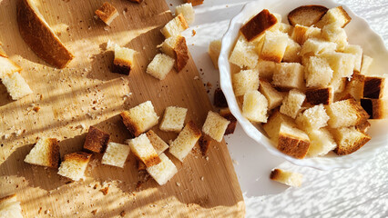 Homemade slices of diced dry white rye bread on cutting board and white plate. Crackers for food, healthy eating on table in sunny day, top view