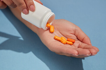 Against the blue background, orange pills are poured from a white bottle unlabeled into a woman's palm. View from above, advertising scene