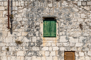 Fototapeta na wymiar Typical old house with weathered closed green wooden shutters and stone wall, Rogoznica village, Dalmatia, Croatia