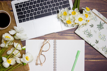 A working items with flowers, computer, notebook and glasses over the wooden background. 
