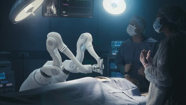 Two Surgeons Observing High-Precision Programmable Automated Robot Arms Operating Patient In High-Tech Hospital. Robotic Limbs Performing Complicated Nanosurgery, Doctors Looking At Vitals On Monitor.