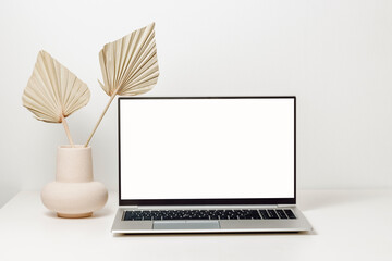 Laptop mockup with white screen and vase with palm leaf on the table. Laptop background for work and study, cozy home office, web site promotion, social media template