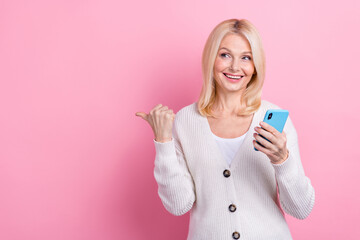 Portrait of charming cheerful person hold telephone look direct finger empty space isolated on pink color background