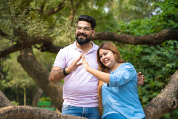 Obraz premium Young indian couple making home shape with hand at park