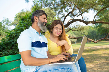 Happy indian Couple using laptop at garden.