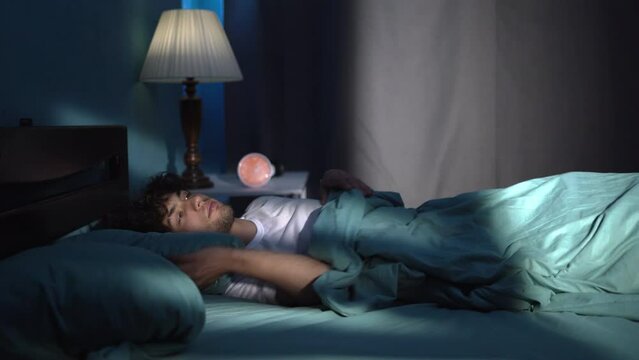 Sleepless and desperate young man suffering from insomnia in stress and sleeping disorder, awake at night not able to sleep