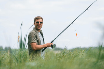 Positive and handsome man in sunglasses is fishing outdoors