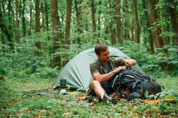 Sitting near the tent. Tourist in summer forest. Conception of exploration and leisure