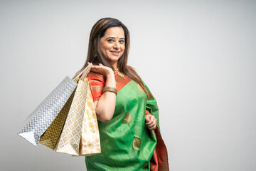 Young Indian woman wearing saree outfit and holding shopping bags on white background.