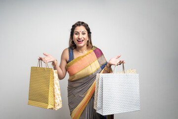 Young Indian woman wearing saree outfit and holding shopping bags on white background.