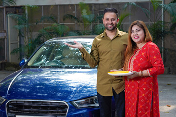 Young indian couple standing with new car. woman holding puja thali in hand.