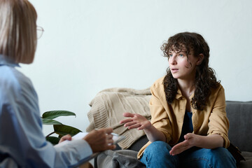 Young woman having consultation with psychologist, they sitting opposite each other and discussing...