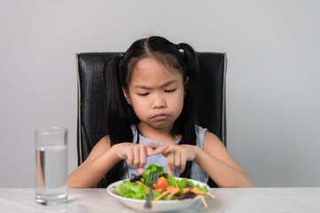 Obraz na płótnie Canvas Little asian cute girl refuses to eat healthy vegetables.Nutrition & healthy eating habits for kids concept.Children do not like to eat vegetables.