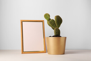 Beautiful cactus in pot and frame on beige table
