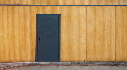 Fototapeta na wymiar Black metal door mounted at wooden wall of warehouse facade outdoor front view