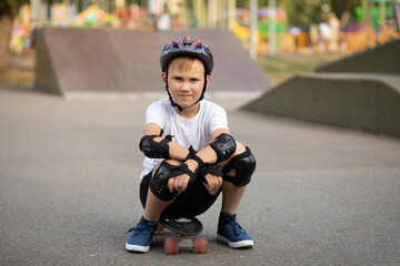 Cute kid boy child in a helmet sitting in a special area in skatepark and holding skateboard....