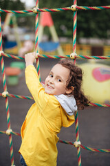 Active little kid girl in yellow raincoat on outdoor playground. Healthy summer activity.