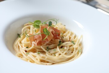 Tasty spaghetti with prosciutto and microgreens on plate, closeup. Exquisite presentation of pasta dish