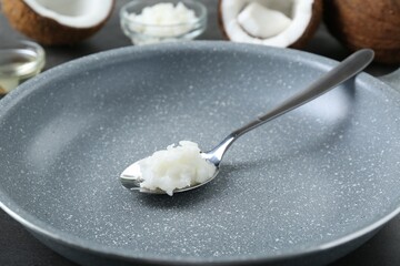 Frying pan with organic coconut cooking oil and spoon on table, closeup