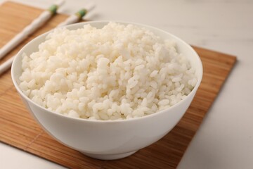 Bowl with delicious rice and chopsticks on white table, closeup