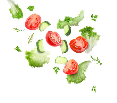 Lettuce leaves, arugula, parsley, cut cucumber and tomatoes falling on white background