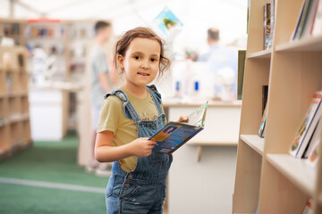 Little cute girl child reading a book on the library or bookstore