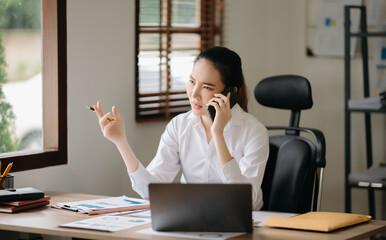 Business asian woman Talking on the phone and using a laptop with a smile while sitting at office..