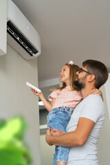 Happy family, father and little girl fun turn on air conditioner using remote control. Cooler system