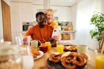 Obraz na płótnie Canvas Happy multiracial couple using mobile phone together over breakfast at home