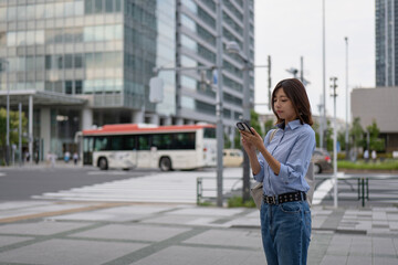 オフィス街の歩道でスマートフォンを見る女性
